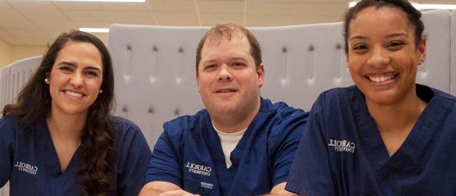 Three smiling healthcare professionals wearing scrubs with 博天堂官方入口登陆登录's logo displayed.