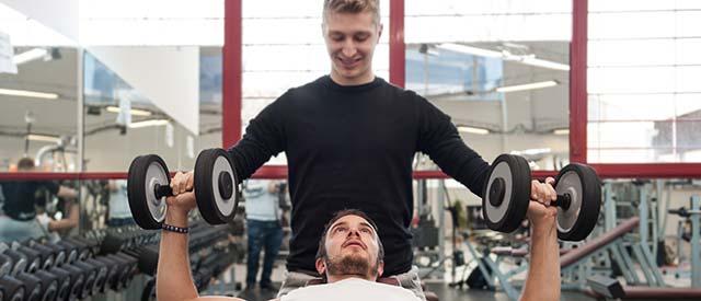 Man lifting weights in gym with trainer